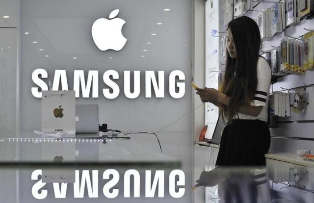 a sales assistant uses her mobile phone next to the company logos of apple and samsung at a store in hefei anhui province september 10 2014 photo reuters