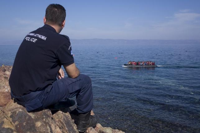 a greek police officer looks at an overcrowded dinghy carrying refugees and migrants arriving on the greek island of lesbos photo reuters