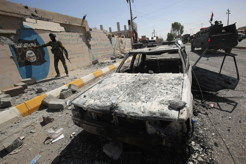 a member of the iraqi government forces point to an islamist flag covered in graffiti near a burnt out vehicle in the town of sharqat around 80 kilometres 50 miles south of the city of mosul on september 23 2016 photo afp