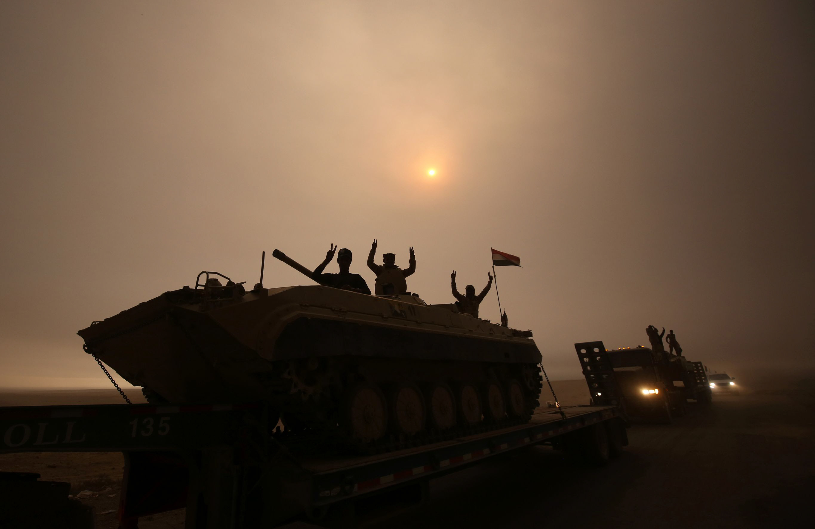 iraqi forces flash the v sign as they stand on an infantry fighting vehicle loaded on a truck driving through the al shura area south of mosul photo afp