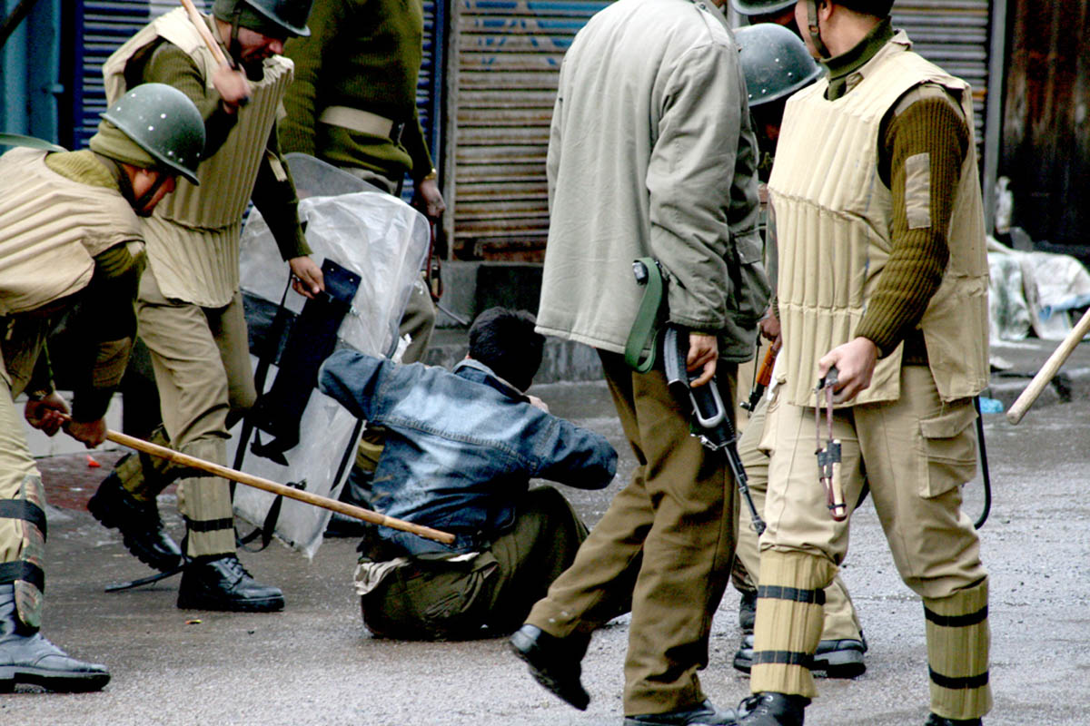 kashmiri protester being beaten by indian security forces with a brick and bamboo sticks as they detain him during a protest in srinagar