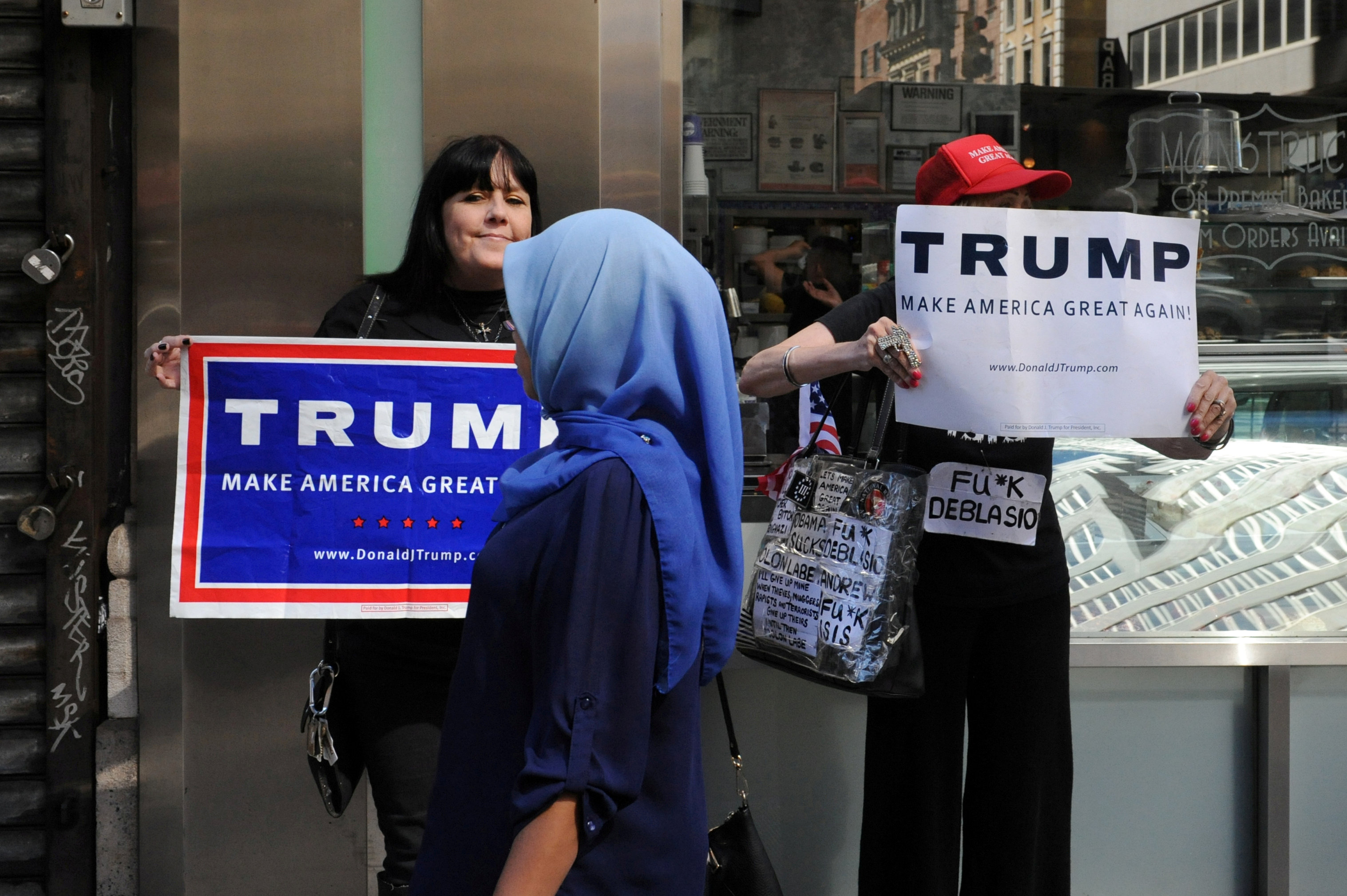 a woman wearing a muslim headscarf walks past people holding u s republican presidential nominee donald trump signs before the annual muslim day parade in the manhattan borough of new york city september 25 2016 reuters stephanie keith file photo