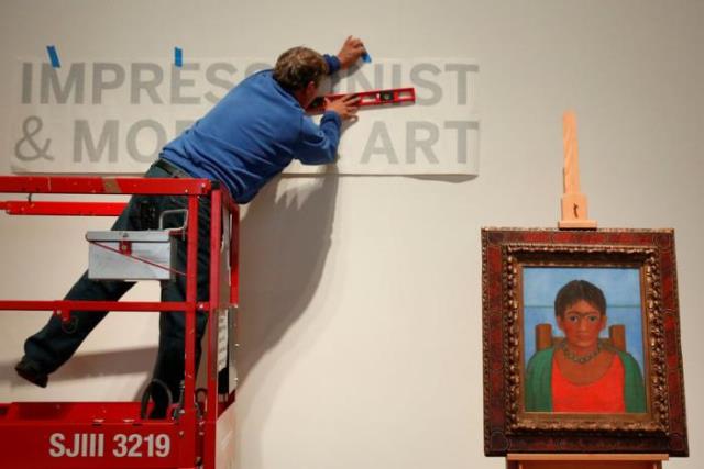 a man hangs a sign as artist frida kahlo 039 s painting 039 nina con collar 039 sits on an easel at sotheby 039 s auction house in new york us november 14 2016 photo reuters