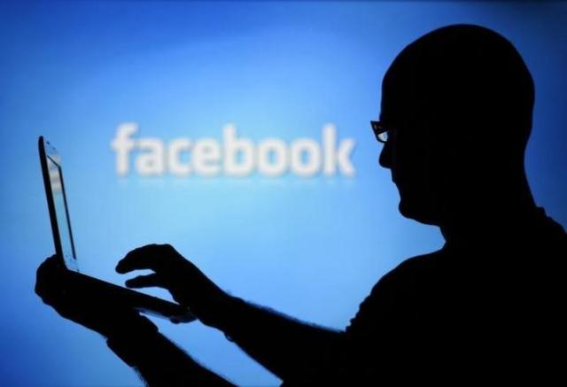 a man is silhouetted against a video screen with an facebook logo photo reuters