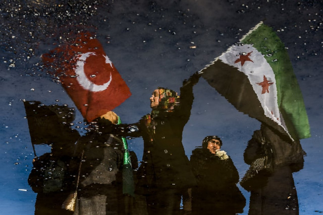 a reflection on waste liquid shows a woman wawing turkish and free syrian flags as an aid convoy to aleppo organised by ihh humanitarian relief foundation is about to leave on december 14 2016 in istanbul photo afp