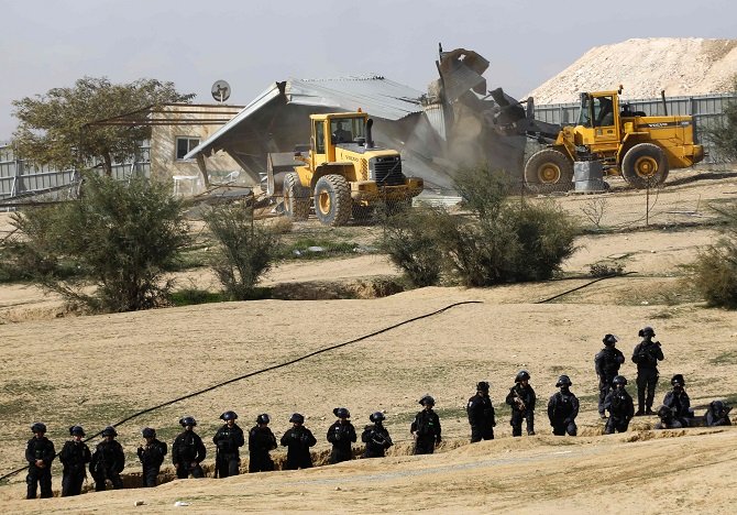 israeli policemen stand guard as bulldozers demolish homes in the bedouin village of umm al hiran which is not recognized by the israeli government near the southern city of beersheba in the negev desert on january 18 2017 photo afp