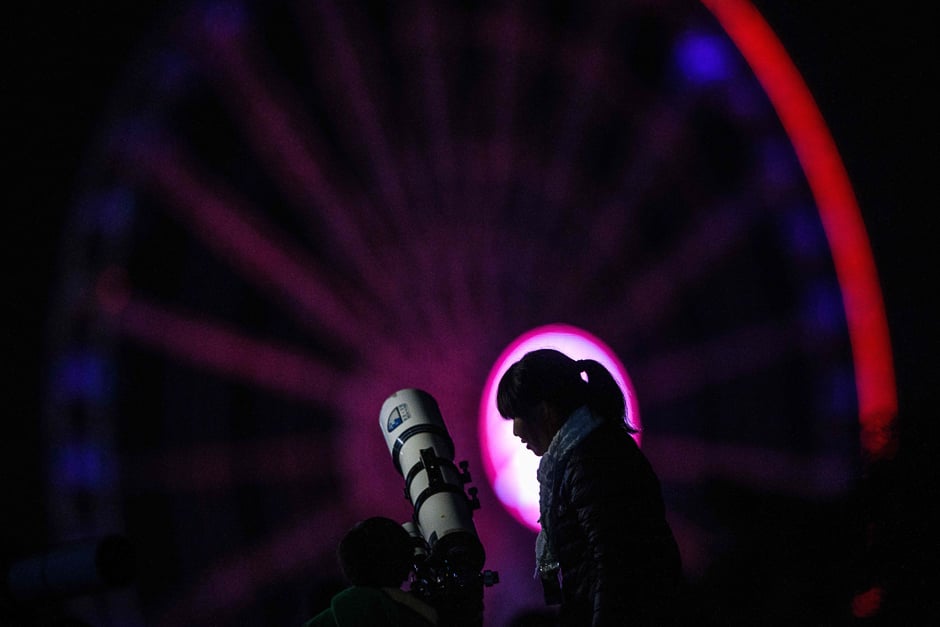 A woman and a child set up a telescope in front of a ferris wheel in the hope of seeing a 'supermoon' on a cloudy evening in Hong Kong. PHOTO: AFP