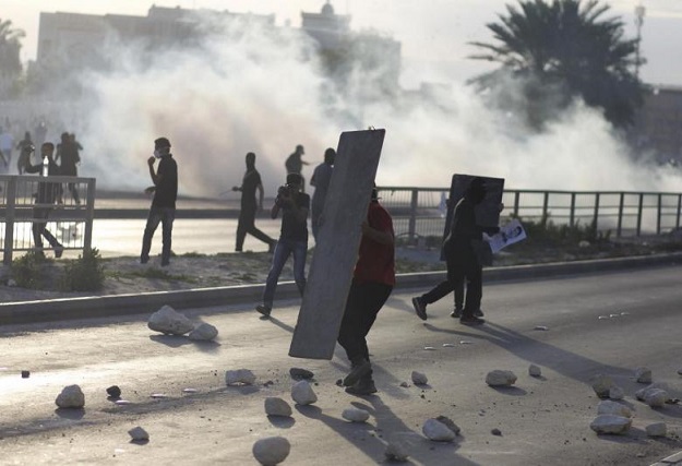 an anti government protester takes cover behind a piece of wood amid teargas fired by riot police during clashes after a revisit to the grave procession of detainee jaffar mohammed jaffar in the village of daih west of manama march 3 2014 an explosion in bahrain killed three police officers during a clash with protesters west of the capital manama on monday the interior ministry said it said on its twitter account that a group of protesters had broken away from a mourning procession in the village of daih and started blocking roads the explosion took place as the policemen were trying to disperse the rioters it added photo reuters