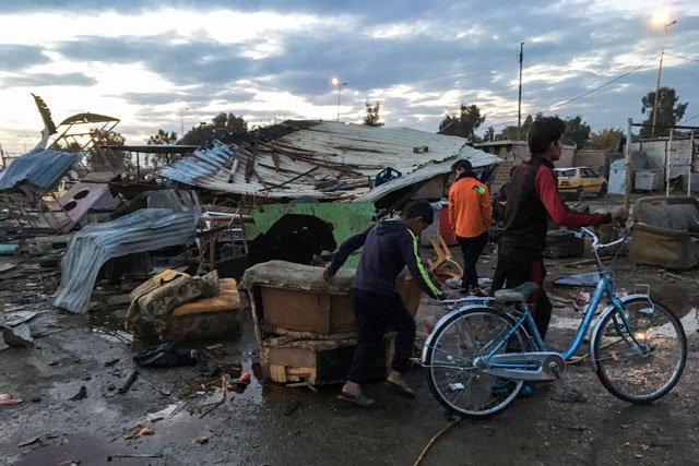 a picture taken with a mobile phone on february 16 2017 shows two iraqi children walking with a bicycle at the scene of a blast by a massive car bomb which killed dozens in a used car market in southern baghdad photo afp