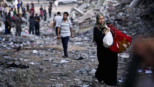 a palestinian woman takes some of her belongings from her partially destroyed home across the street photo afp