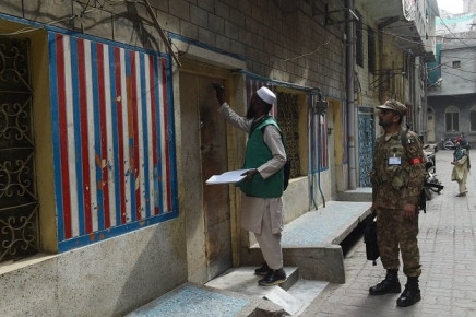 an official from the pakistan bureau of statistics l marks a house after collecting information from a resident during a census as army slodier stands guard in lahore on march 15 2017 photo afp