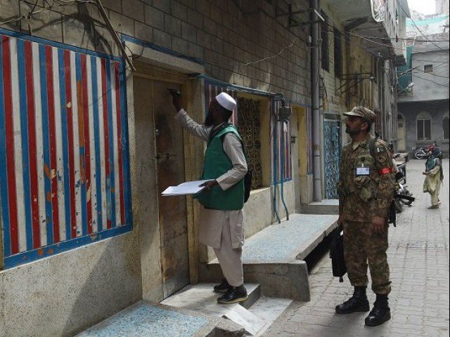 an official from the pakistan bureau of statistics l marks a house after collecting information from a resident during a census as army slodier stands guard in lahore on march 15 2017 photo afp