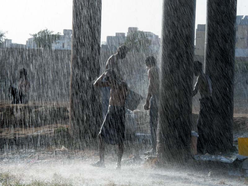 residents take a shower under a leaking water pipeline in karachi photo afp