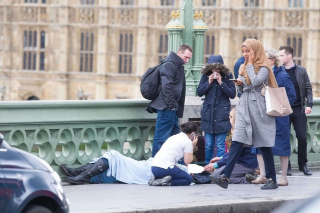 a hijab clad woman walks past a group of people helping a victim photo twitter a hijab clad woman walks past a group of people helping a victim photo twitter