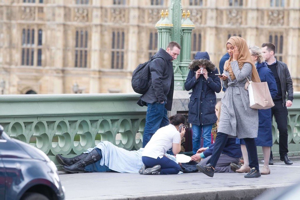 a hijab clad woman walks past a group of people helping a victim photo twitter