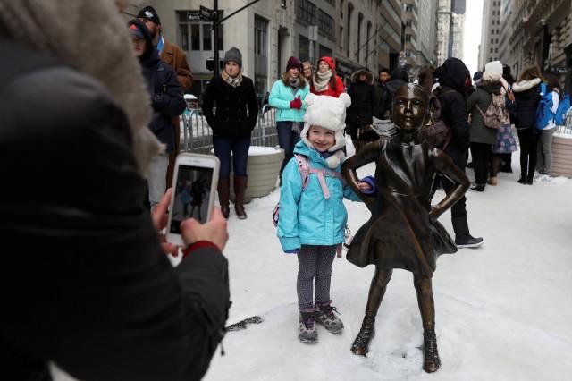 a girl has her picture taken with the 039 fearless girl 039 statue which stands in front of wall street 039 s charging bull statue is seen in new york us photo reuters