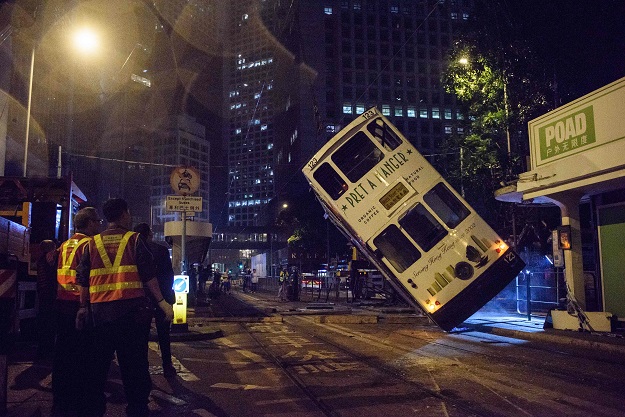 emergency service personnel watch as a double decker tram is lifted by crane after it tipped over on a main road in hong kong early on april 6 2017 photo afp