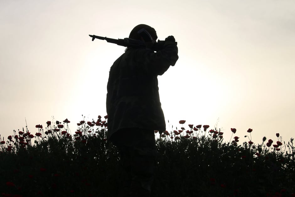 an opposition fighter walks in a field of poppies in a rebel held area in the southern syrian city of daraa photo afp