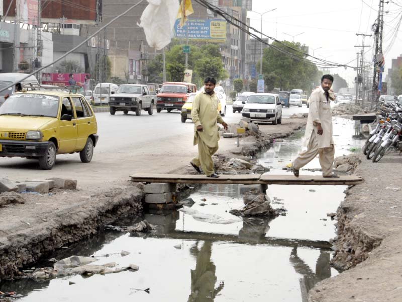 pedestrians use wooden planks to cross over an open drainage photo express