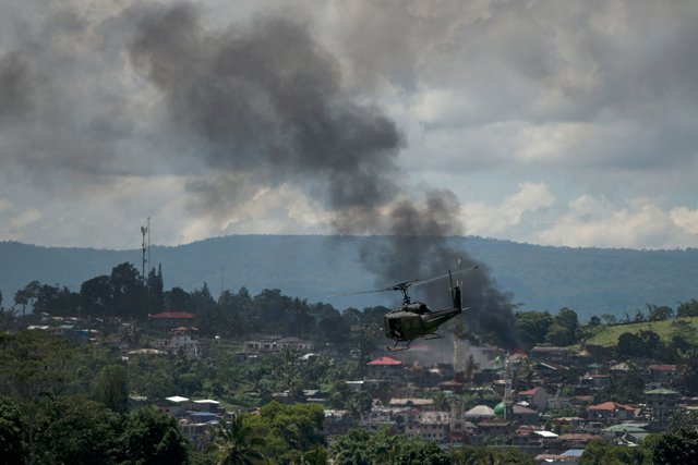 a helicopter flies through smoke billowing from houses after aerial bombings by philippine airforce planes on islamist militant positions in marawi on the southern island of mindanao on june 17 2017 philippine troops pounded islamist militants holding parts of southern marawi city with air strikes and artillery on june 17 as more soldiers were deployed and the death toll rose to more than 300 after nearly a month of fighting photo afp