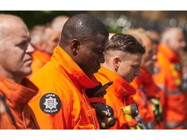 members of london 039 s emergency services observe a minutes 039 silence in memory of the victims of the june 14 fire at the grenfell tower block pictured on the horizon in kensington west london on june 19 2017 photo afp