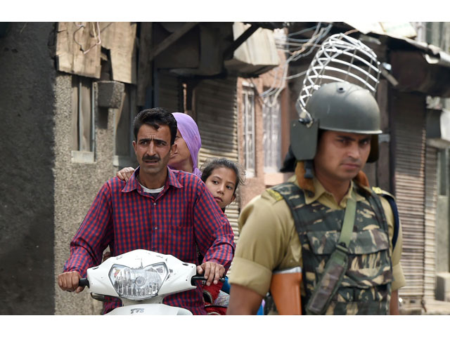 an indian paramilitary trooper stands guard as a kashmiri family rides past in srinagar on july 21 2017 photo afp