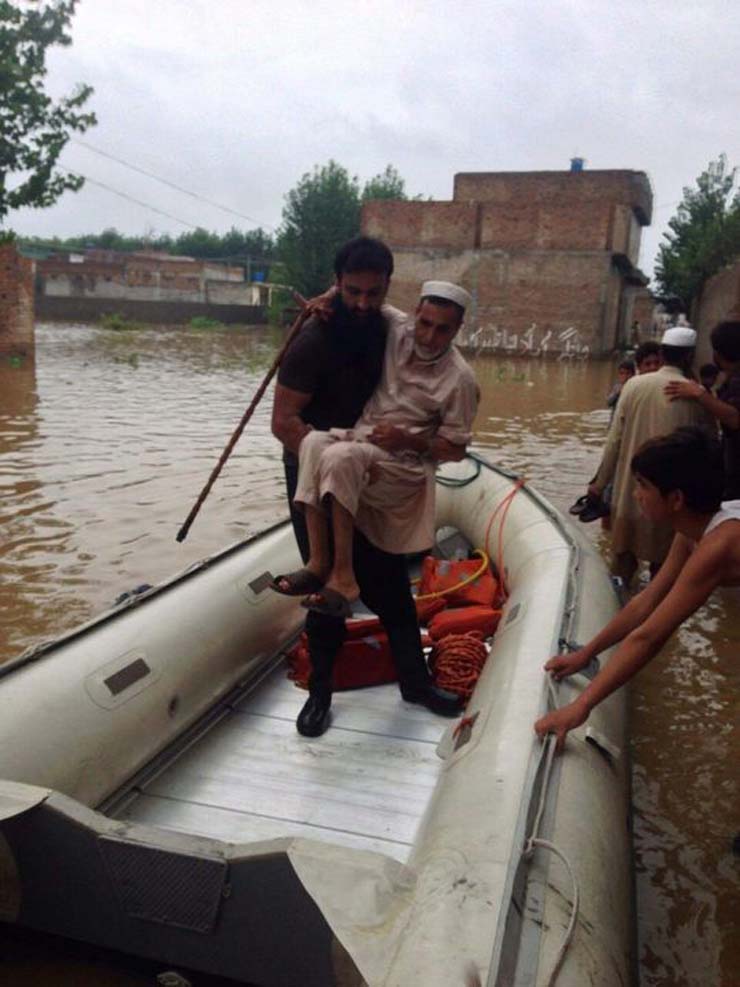 a rescue 1122 official helps a man into a rescue boat in flooded charsadda photo rescue 1122
