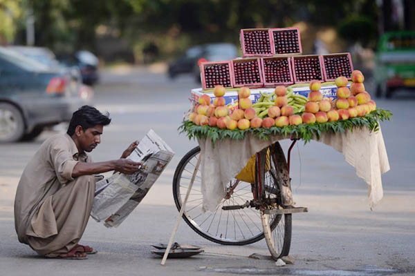 a fruit vendor reads a newspaper as he waits for customers on a street in islamabad photo afp