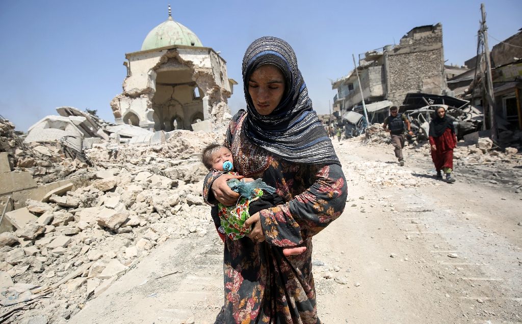 an iraqi woman carrying a child walks by the destroyed al nuri mosque as she flees the old city of mosul photo afp