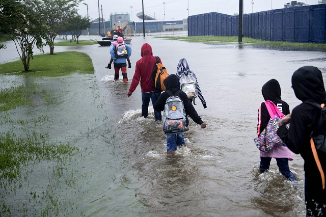 people walk to a harris county sherif air boat while escaping a flooded neighborhood during the aftermath of hurricane harvey on august 29 2017 in houston texas floodwaters have breached a levee south of the city of houston officials said tuesday urging residents to leave the area immediately photo afp
