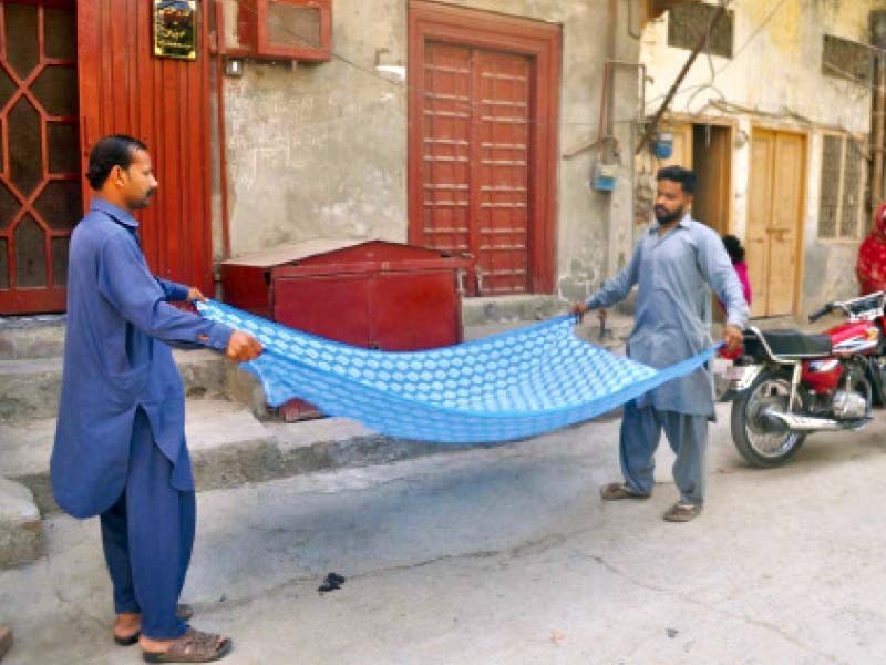 two men dry a dupatta left while their colleague dyes one more for them to dry right photo express