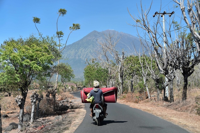 villagers transport a mattress back to their home in kubu village near the base of mount agung volcano in background in karangasem regency on the indonesian resort island of bali on september 27 2017 photo afp