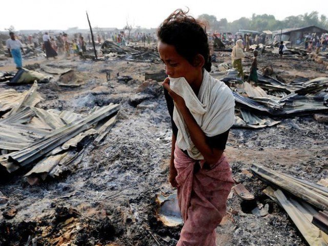 a woman walks among debris after fire destroyed shelters at a camp for internally displaced rohingya muslims in the western rakhine state near sittwe in myanmar photo reuters