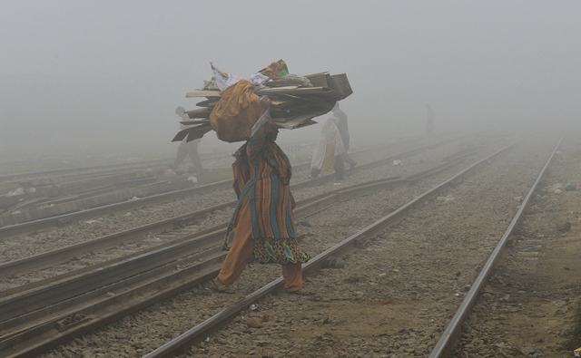 a woman holds a cardboard on her head as she crosses a rail track in heavy smog in lahore photo afp