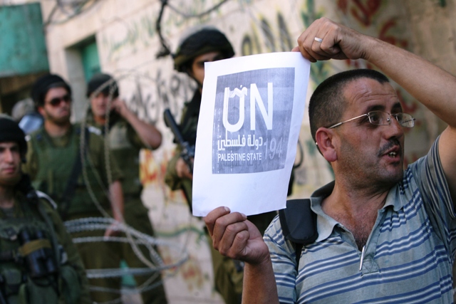 a palestinian man holds up a sign in support of the palestinian request for un membership during a protest at an israeli army checkpoint in the centre of the divided west bank city of hebron on september 14 2011 photo afp