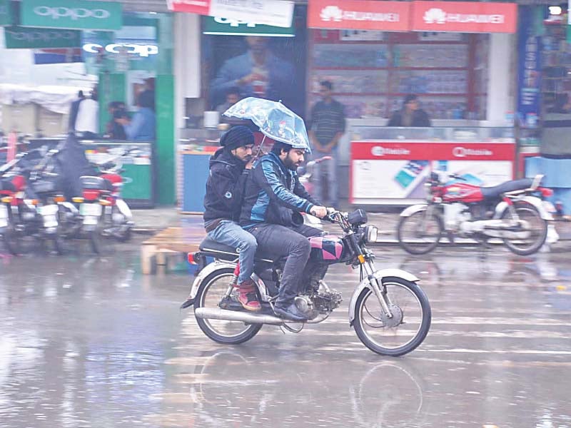 motorcyclists pass through a road during rain in faisalabad photo online