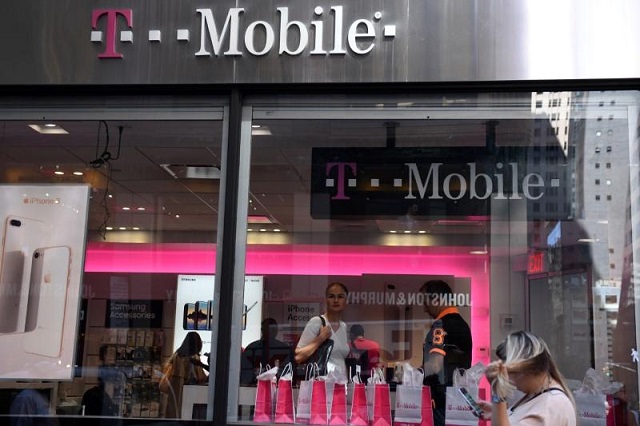 a pedestrian uses her smart phone as she passes a t mobile retail store in manhattan new york us september 22 2017 photo reuters