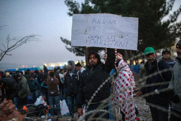 a migrant from pakistan holds a placard as he waits with other migrants and refugees to cross the greek macedonian border near gevgelija on november 20 2015 photo afp a migrant from pakistan holds a placard as he waits with other migrants and refugees to cross the greek macedonian border near gevgelija on november 20 2015 photo afp