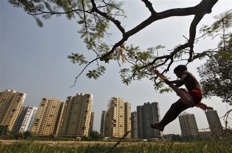 a boy plays on a swing suspended from a tree in front of a residential estate under construction photo reuters
