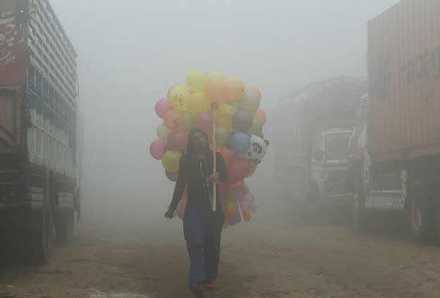 a pakistani vendor carries baloons on a street amid heavy smog in lahore photo afp