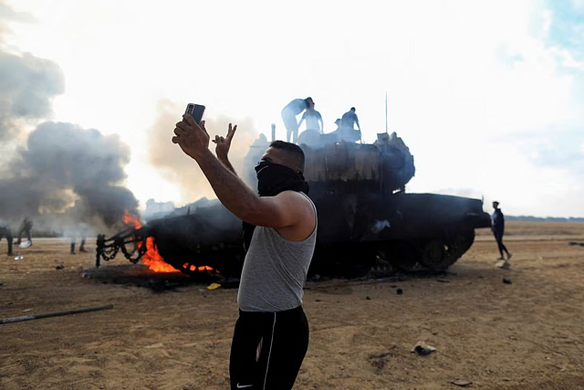 A Palestinian man takes a selfie in front of a burning Israeli military vehicle after it was hit by Palestinian gunmen who infiltrated areas of southern Israel, at the Israeli side of Israel-Gaza border, October 7, 2023. REUTERS