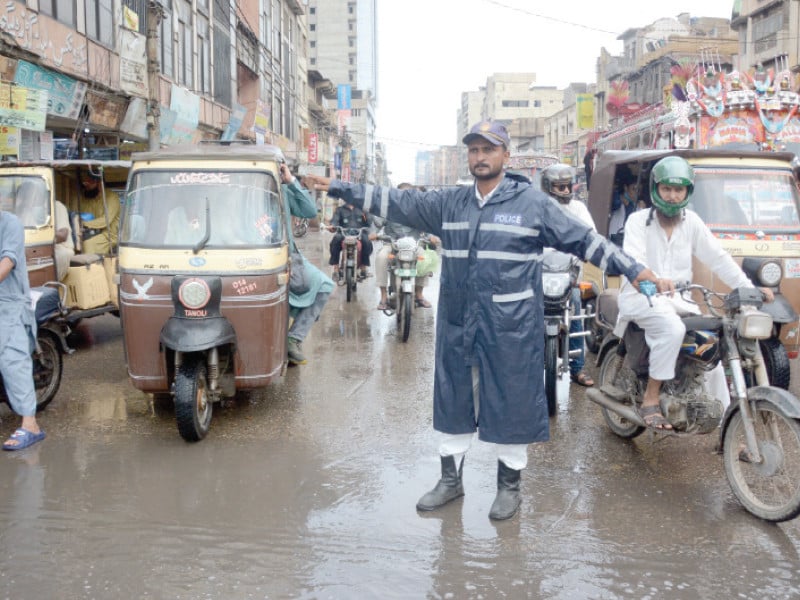 a constable wearing a raincoat performs duty to maintain swift flow of traffic in saddar photo express