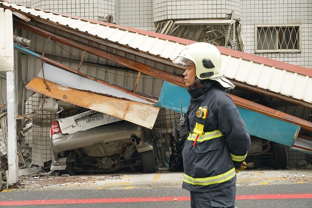 a rescue worker stands next to a crushed car l the morning after a 6 4 magnitude quake hit the eastern taiwanese city of hualien on february 7 2018 rescue workers scrambled to search for survivors in buildings left tilting precariously on their foundations in the taiwanese city of hualien on february 7 after an overnight earthquake killed four and injured more than 200 photo afp