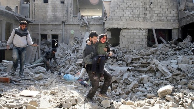 a man carries an injured boy as he walks on rubble of damaged buildings in the rebel held besieged town of hamouriyeh eastern ghouta near damascus syria february 21 2018 photo reuters