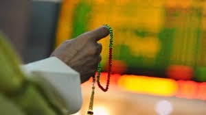 an investor holds the tasbeeh as he monitors electronic boards displaying stock information photo reuters