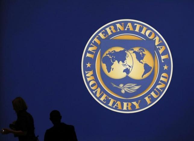 visitors are silhouetted against the logo of the international monetary fund imf in tokyo photo reuters