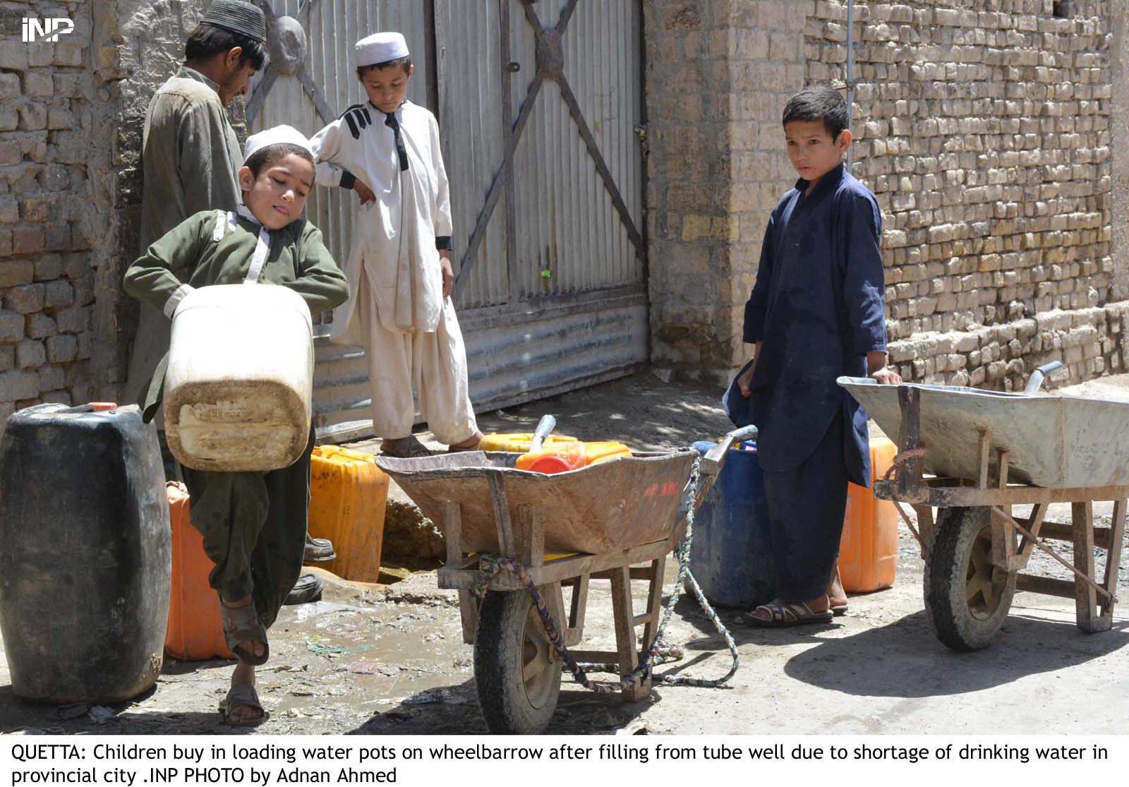 a kid uses his knee to lift a water gallon up for putting it in a cart in quetta photo inp