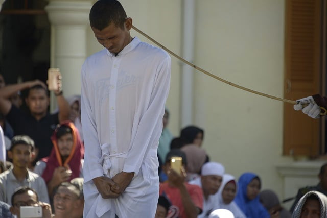 a member of indonesia 039 s sharia police whips a man l accused of having gay sex during a public caning ceremony outside a mosque in banda aceh capital of aceh province on july 13 2018 photo afp