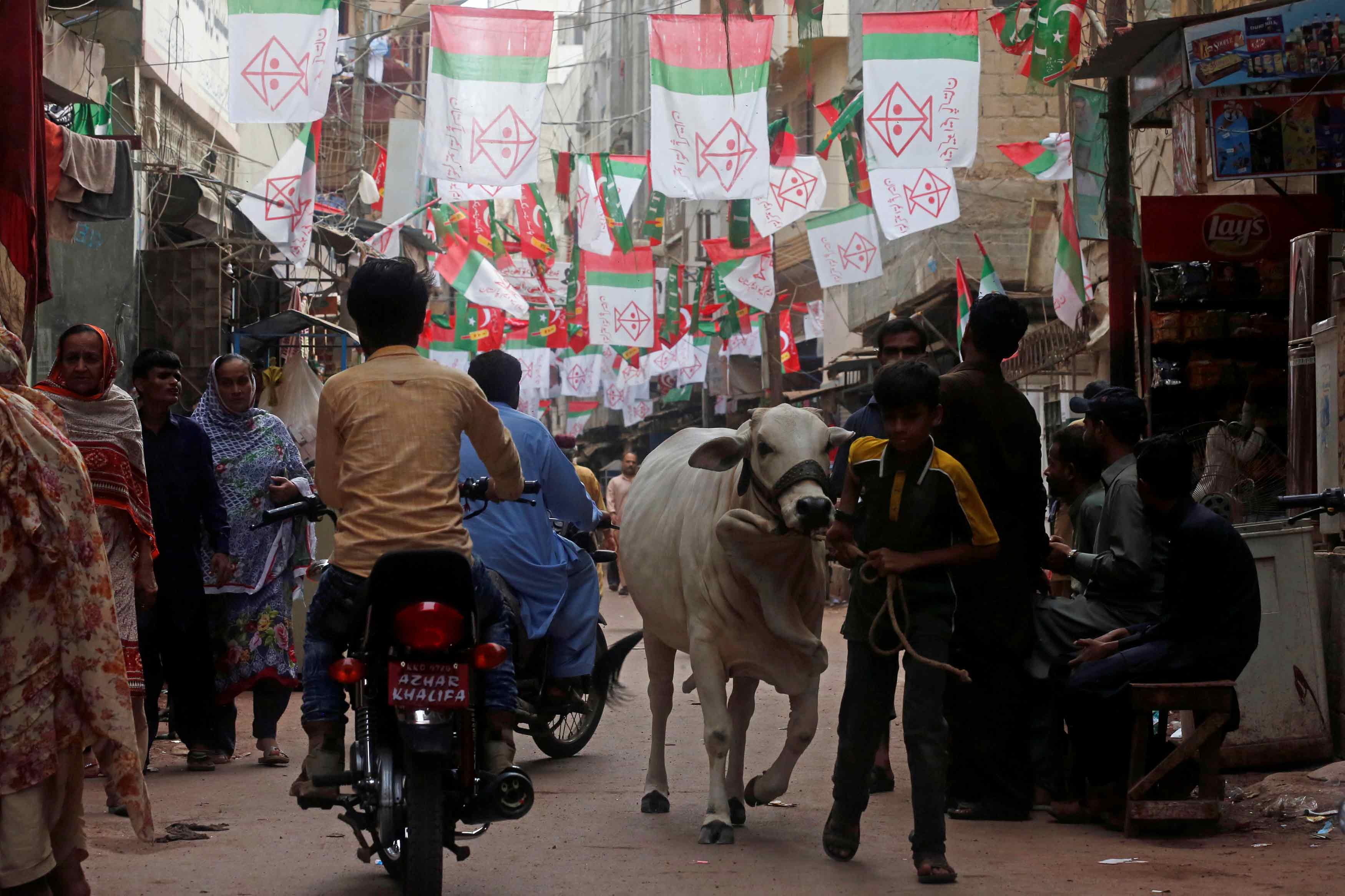 residents walk along a street decorated with flags of political parties ahead of general elections in the lyari neighborhood in karachi photo reuters