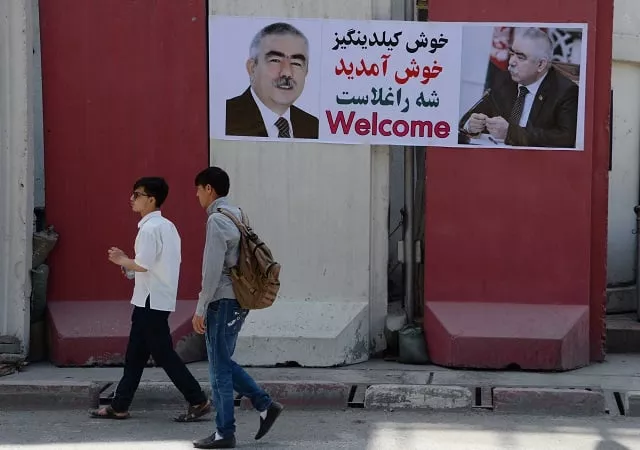 afghan residents walk past a banner with the image of self exiled afghan vice president abdul rashid dostum ahead of his arrival to kabul on july 22 2018 dostum is expected to return to kabul on july 22 more than a year after fleeing the country during an investigation into the rape and torture of a political rival photo afp